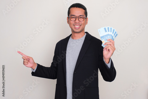 Asian casual businessman smiling and pointing to the right side while holding money photo