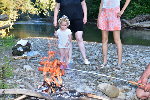Obraz na płótnie The family is camping by the river and roasting sausage over a natural fire w salonie