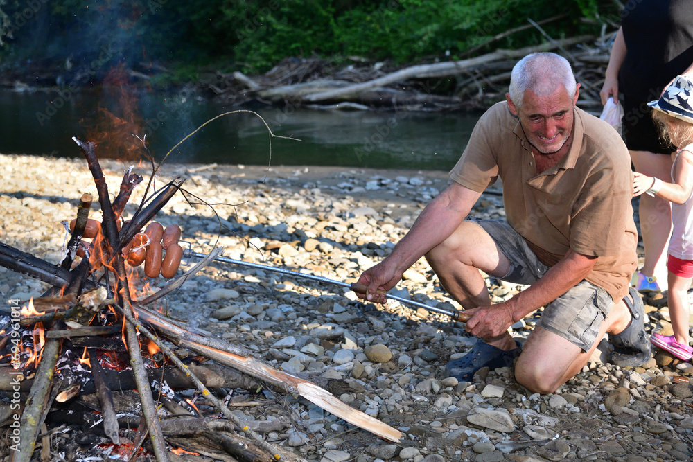 A man roasts a pile of sausages on a stick over a natural fire