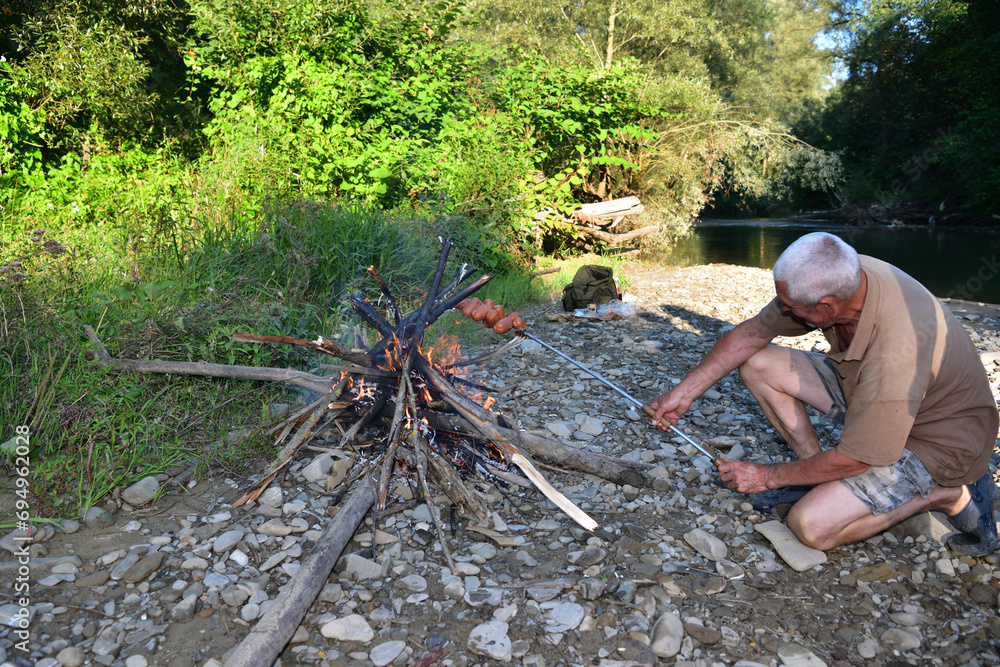 A man roasts a pile of sausages on a stick over a natural fire