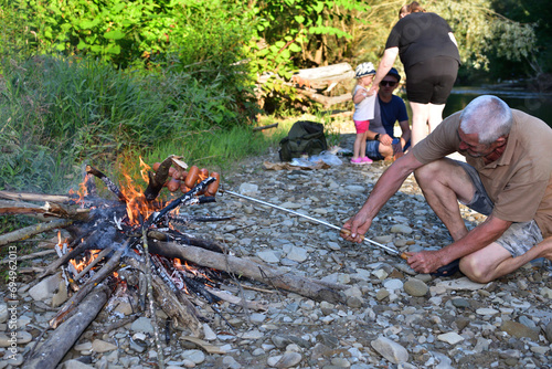 Obraz na płótnie The family is camping by the river and roasting sausage over a natural fire w salonie