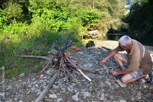 Obraz na płótnie A man roasts a pile of sausages on a stick over a natural fire w salonie