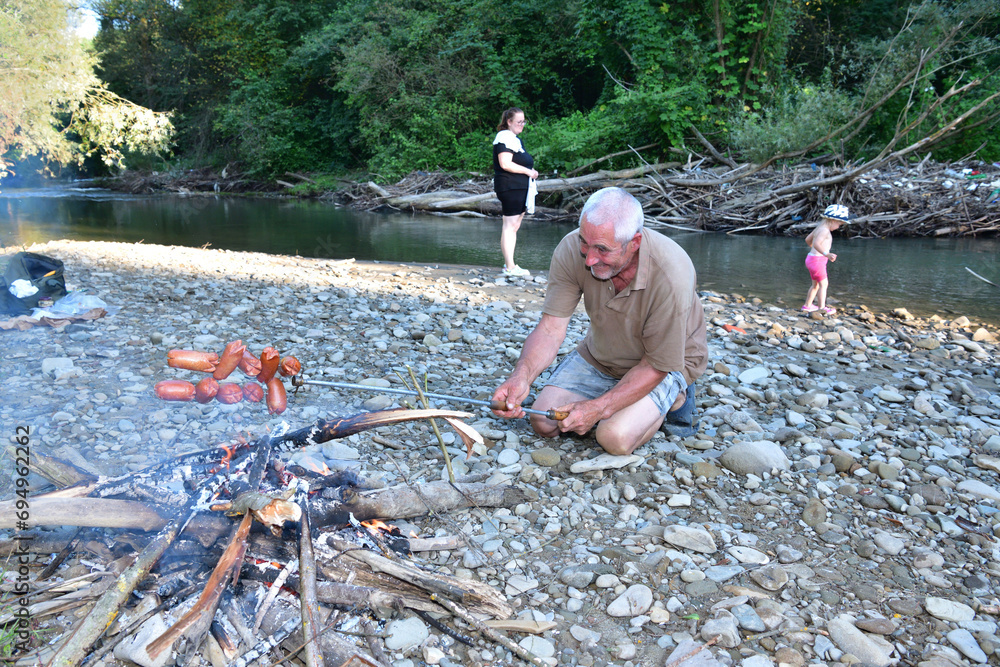 A man roasts a pile of sausages on a stick over a natural fire