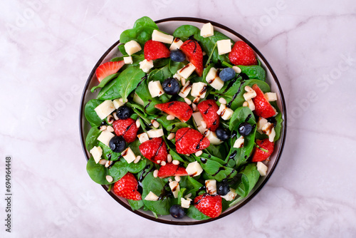 Salad with strawberry, spinach, blueberry, caciotta cheese and pine nuts dressed with balsamic glaze. Healthy meal. Top view photo