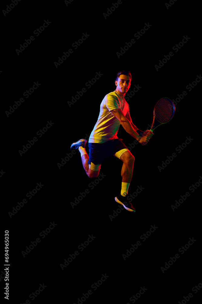 Dynamic image of man, tennis player in motion with racket against dark background in neon light. Concept of professional sport, competition, game, math, hobby, action Dynamic image of man, tennis player in motion with racket against dark background in neon light. Concept of professional sport, competition, game, math, hobby, action