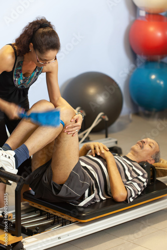 Fototapeta Naklejka Na Ścianę i Meble -  sick old man doing therapy recovery on a pilates machine with a female therapist, balls in the background