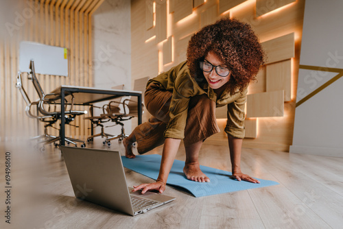 Woman practicing yoga at office using online lesson standing on a mat
