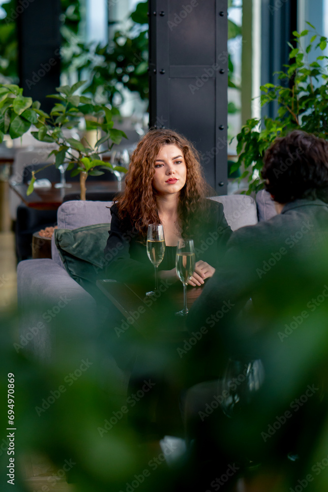Fototapeta premium portrait of young upset curly woman quarreling on business meeting with colleague or on date with man with glasses of champagne