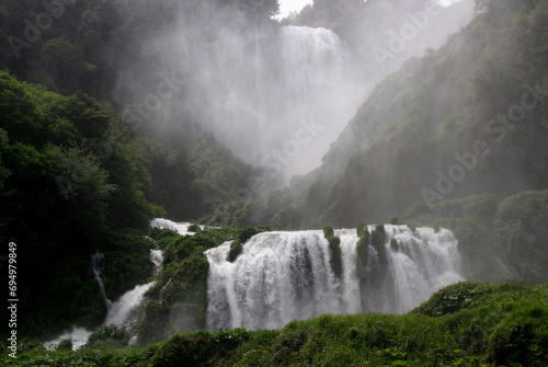 Landscape view of Cascata delle Marmore cascading waterfall and mist from water splashes around it in Marmore town, Terni, Umbria region, Italy photo