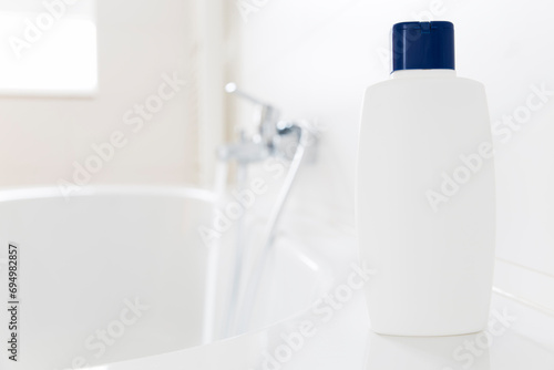 White bottle of shampoo standing on a bathtub in a bright bathroom