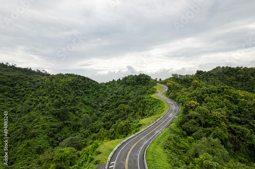 Aerial view of countryside road passing through the green forest and mountain in Thailand.