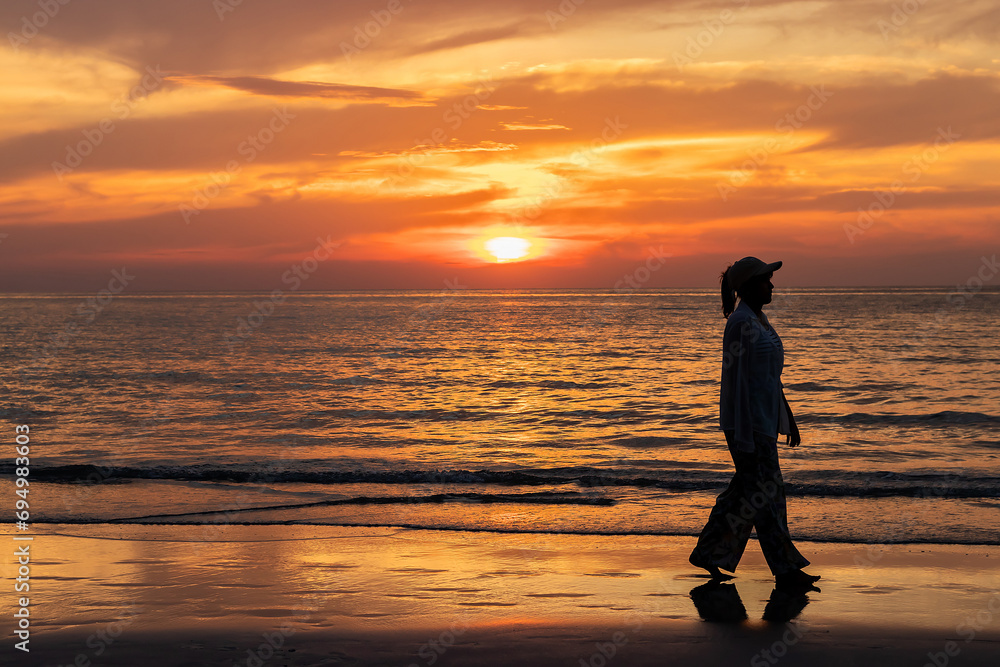 Happy young asian woman walking alone on a beach at sunset.