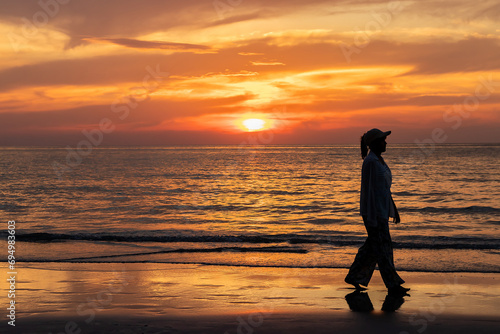 Happy young asian woman walking alone on a beach at sunset.