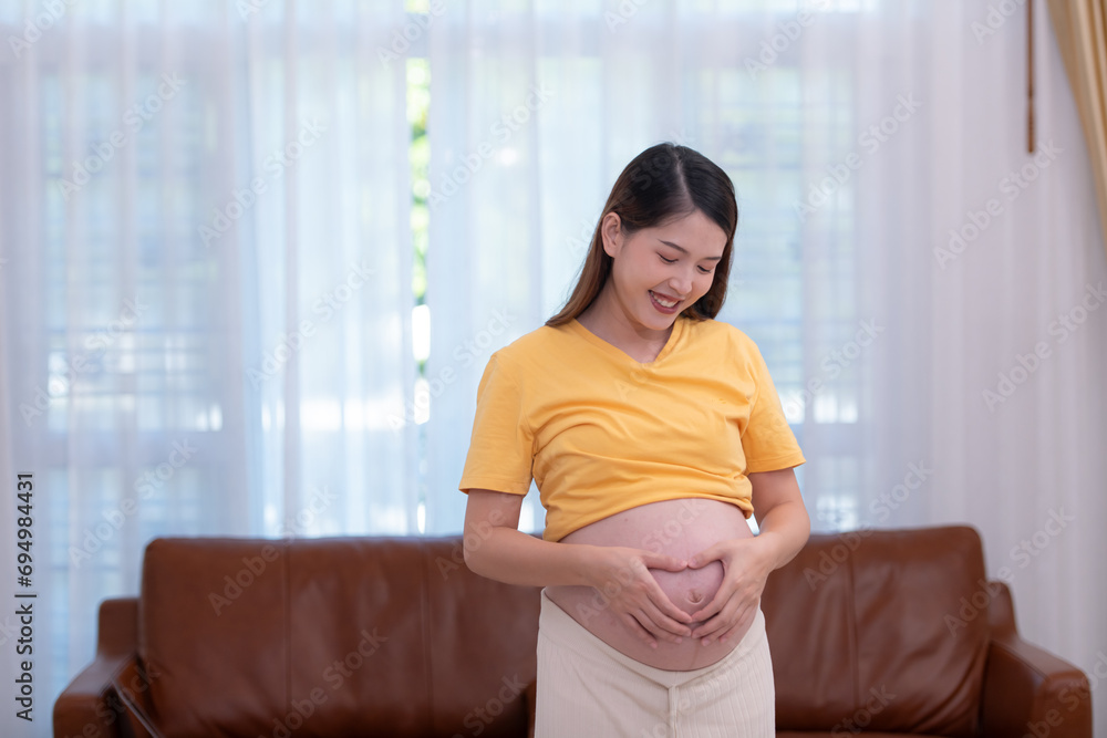A pregnant woman feels happy at home while taking care of her baby in the womb. Young mother showing signs of love to her baby in the womb A pregnant woman feels happy at home while taking care of her baby in the womb. Young mother showing signs of love to her baby in the womb