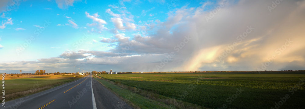 Panoramic view of a road and an agricultural field under forming clouds