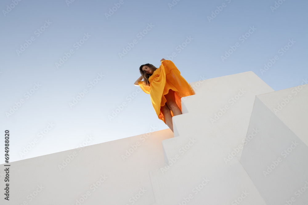 Fototapeta premium Girl in orange dress on white background with blue sky