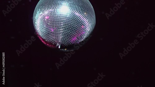 Silver mirror disco ball suspended from the ceiling rotates quickly, light spot rays and glare. White stage light at a concert hall, club, party or disco. Illumination and atmosphere. photo