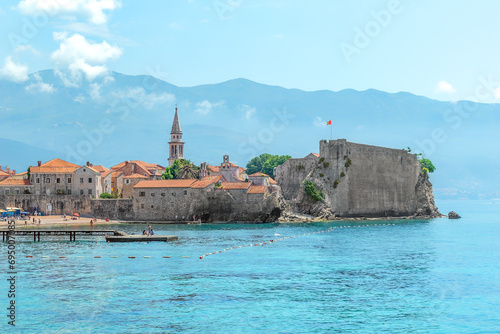 Seascape with the fortress of the Old Town of Budva and the spire of the chapel of The Church of Sveti Ivan, Montenegro. Plaza Ricardova Glava beach and Adriatic Sea coastline in a tourist city photo
