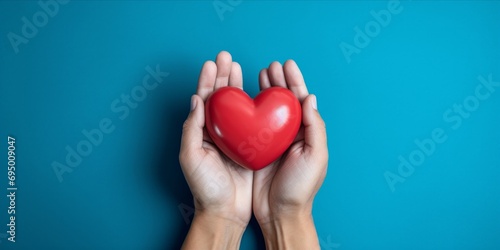 Hands holding a red heart against a blue background.