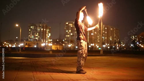 Guy juggles burning pois spinning and rotating it around body. photo