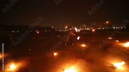 Boy dances juggling burning pois and jumps at evening fire show. photo