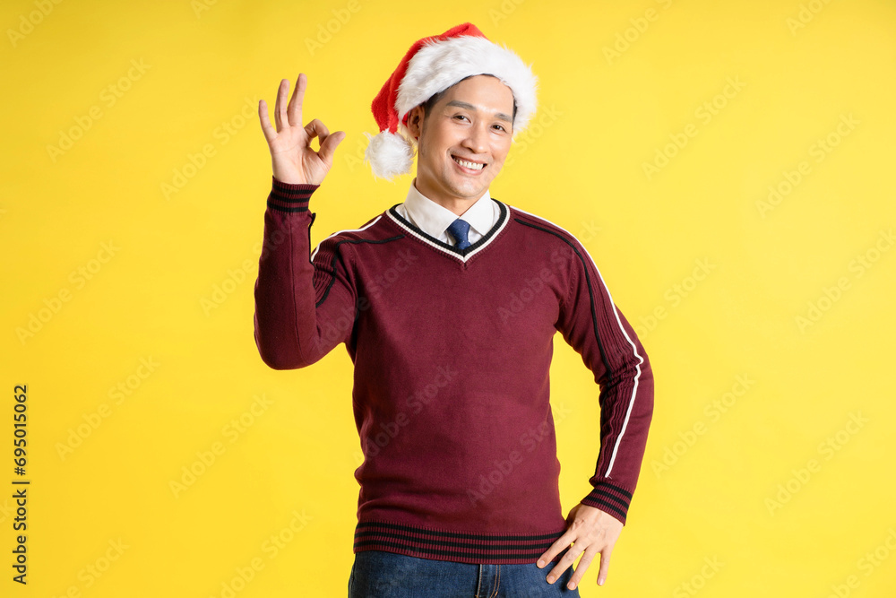 Portrait of an Asian man wearing a Christmas sweater and hat posing on a yellow background Portrait of an Asian man wearing a Christmas sweater and hat posing on a yellow background