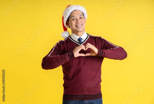Portrait of an Asian man wearing a Christmas sweater and hat posing on a yellow background