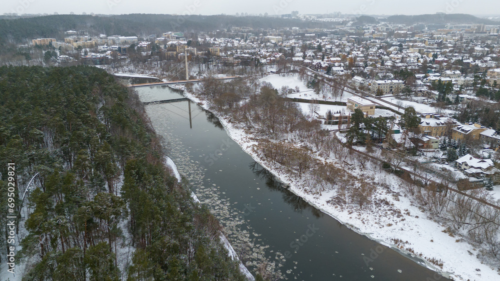 Drone photography of houses in a city near a pine forest park and river during winter