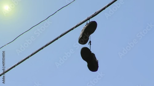Pair of Shoes Dangling from Telephone Wires Against Blue Sky. 4K Resolution. photo