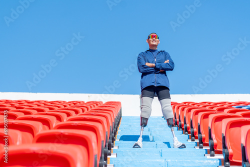 Sport man athlete prosthesis legs stand with arm crossed on stairs with happiness on amphitheater in the stadium with day light.