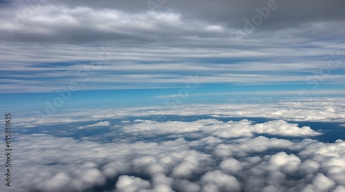 Aerial view of the sky through an airplane window, showcasing fluffy white clouds and a vast blue expanse. Aerial view of white fluffy clouds in the blue sky.