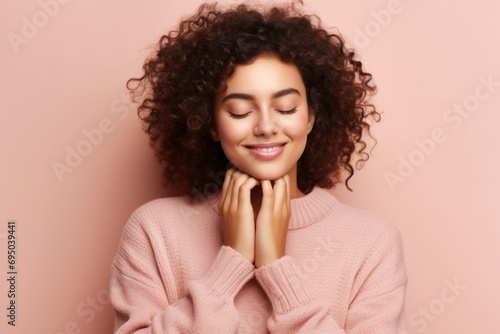 Young beautiful woman with curly hair wearing casual sweater over isolated pink background smiling with hands on chest with closed eyes and grateful gesture on face, Copy space Health concept. photo