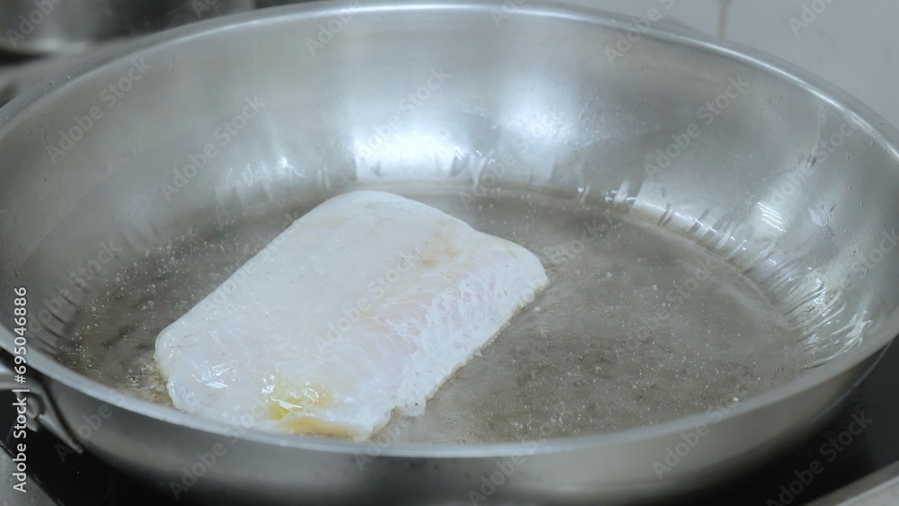 Roasting fish in the kitchen. The cook is frying fish in a frying pan close-up, the chef is cooking in the kitchen, a frying pan with fish, food preparation in a restaurant. Roasting fish in the kitchen. The cook is frying fish in a frying pan close-up, the chef is cooking in the kitchen, a frying pan with fish, food preparation in a restaurant.