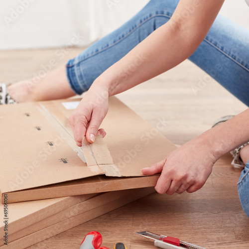 A woman sitting on the floor and opening a cardboard box with self-assembly furniture.