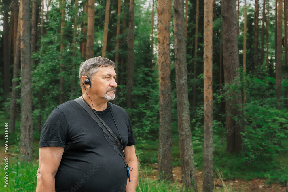 Portrait of a man in his 70s with a radio guide earpiece in the woods. Travelling pensioners. Konevets Island, Karelia, Ladoga Lake Portrait of a man in his 70s with a radio guide earpiece in the woods. Travelling pensioners. Konevets Island, Karelia, Ladoga Lake