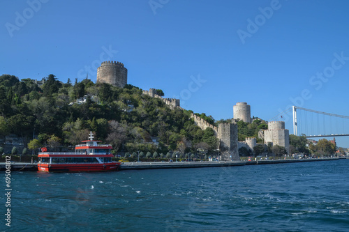 Rumeli Hisari and the Fatih Sultan Mehmed Bridge tower over Turkey’s sparkling Bosphorus as a red ferry docks along the European side