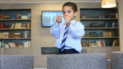 Cute boy in business clothing hides behind armchair and attacks photo