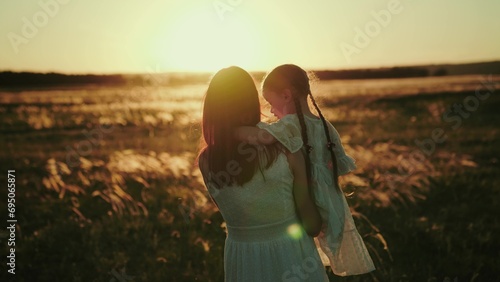 Momma shows daughter to walk on field at sunset. Momma carries daughter in arms after active games on field and at time of sunset. Long haired momma carries little girl after play volleyball on field photo