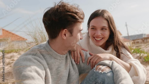 A delightful moment captured as a young woman and a handsome man share laughter while sitting on a sandy beach on a sunny day. Closeup shot of happiness