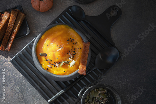 Delicious pumpkin soup with thick cream and sesame and pumpkin seeds on a dark rustic wooden table with toast.
