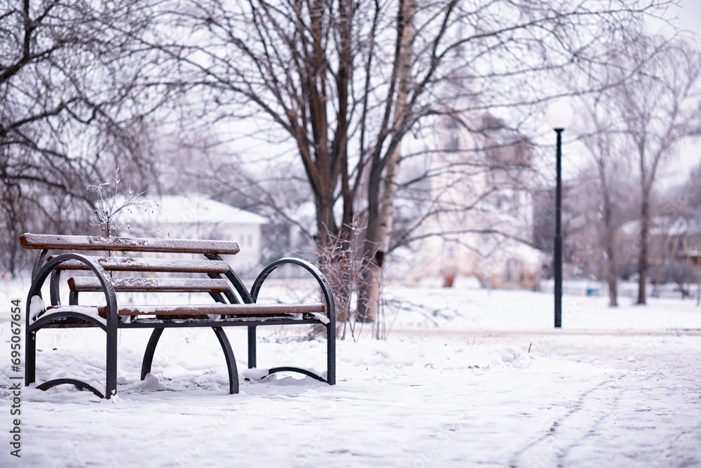 park bench on a winter alley at snowfall. bench with snow after snowstorm or in snow calamity in europe park bench on a winter alley at snowfall. bench with snow after snowstorm or in snow calamity in europe