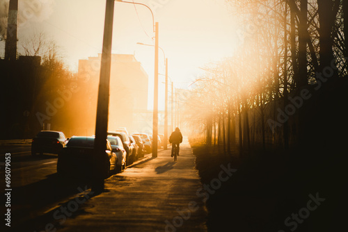 An urban landscape illuminated by the bright morning sun, where a lonely man rides a bicycle to work on a foggy morning. Lifestyle. A shadow.