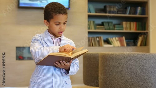 Mulatto boy in striped jacket holds book in hand and reads photo