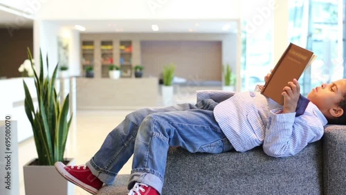 Curly boy lying on sofa with book in business center  photo