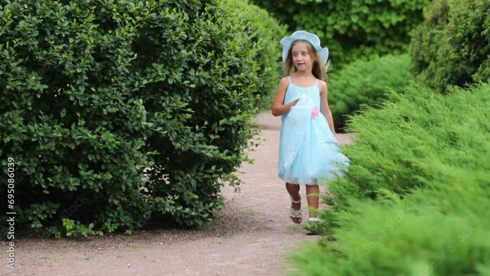 little girl goes on path and turns near bushes in summer park little girl goes on path and turns near bushes in summer park