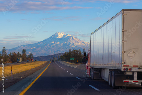 A semi tractor trailer truck drives on the Interstate in California with Mount Shasta in the distance at Sunset.  photo