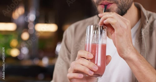 Camera view of man holding glass of freshly squeezed fruit juice or smoothie. Guy drinking delicious drink with straw. Enjoying tasty tipple in cafe or bar. Taste. Organic drink concept.