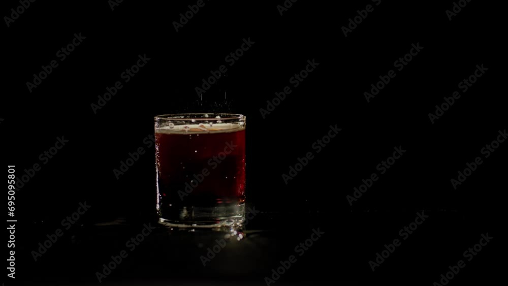 Ice cubes are falling down into the glass with coke on the black background. Closup of the glass with coke into which pieces of ice are falling down. Coke is splashing out on the table. Ice cubes are falling down into the glass with coke on the black background. Closup of the glass with coke into which pieces of ice are falling down. Coke is splashing out on the table.