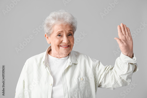 Senior woman waving hand on grey background