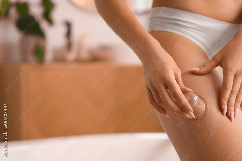 Young woman massaging her thigh with anti-cellulite cup in bathroom, closeup - obrazy, fototapety, plakaty 